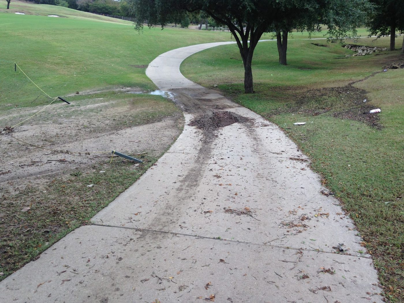 A paved path eroded and covered in debris from unchecked water runoff