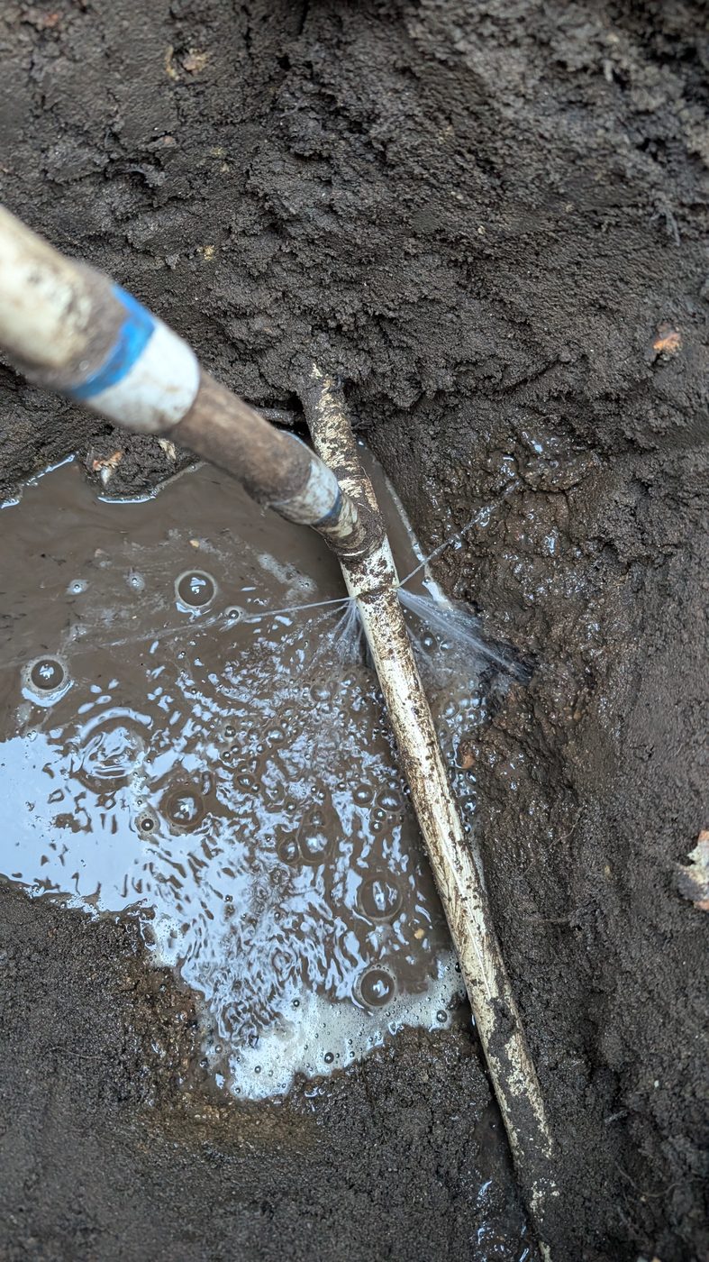 A broken irrigation pipe leaking underground, exposed in a muddy hole